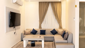 Una sala de estar moderna con un sofá, una mesa de centro, un televisor montado en la pared y una ventana con cortinas.