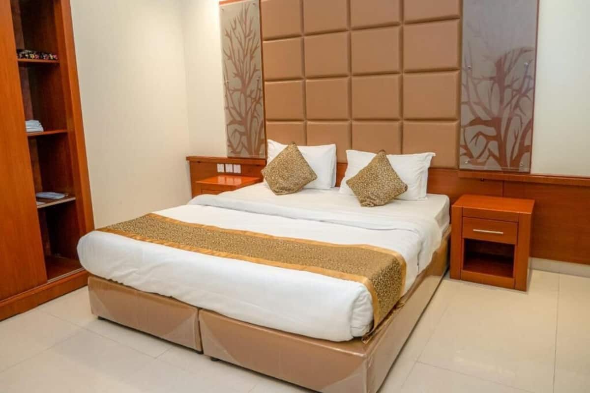 Una habitación de hotel con una cama grande, cabecera de madera, dos mesitas de noche y un armario.