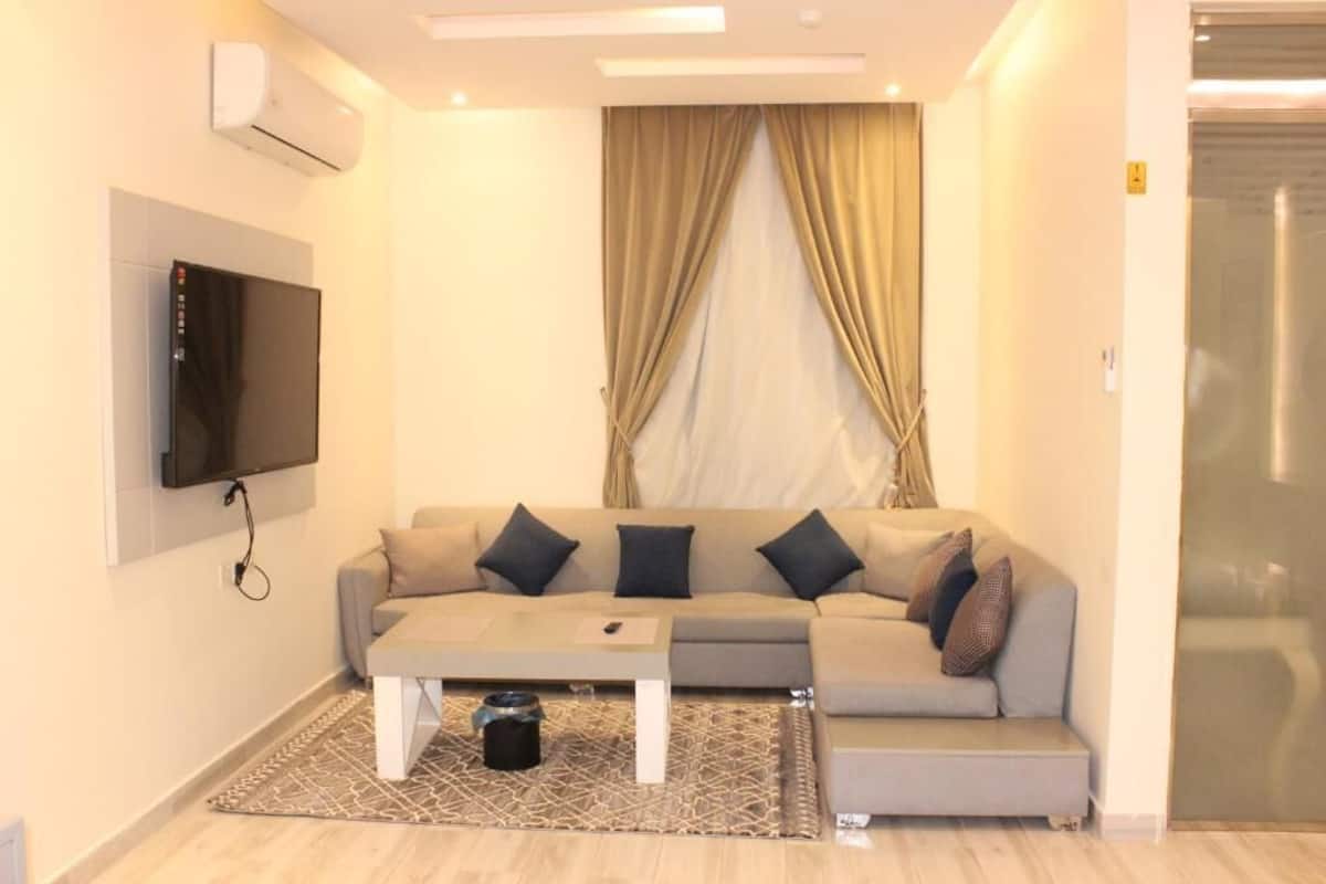 Una sala de estar moderna con un sofá, una mesa de centro, un televisor de pantalla plana montado en la pared y un ventanal corredizo.