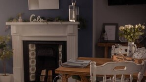 Un comedor con chimenea, mesa de madera y sillas blancas.