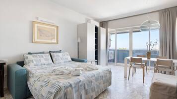 Een moderne hotelkamer met een bed, een slaapbank, een eettafel met stoelen, een balkon met uitzicht en een groot raam.