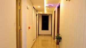 A hotel hallway with a marble floor, a potted plant, a wall-mounted light fixture, and a door at the end. - Hotel Zen Inn (New Delhi)