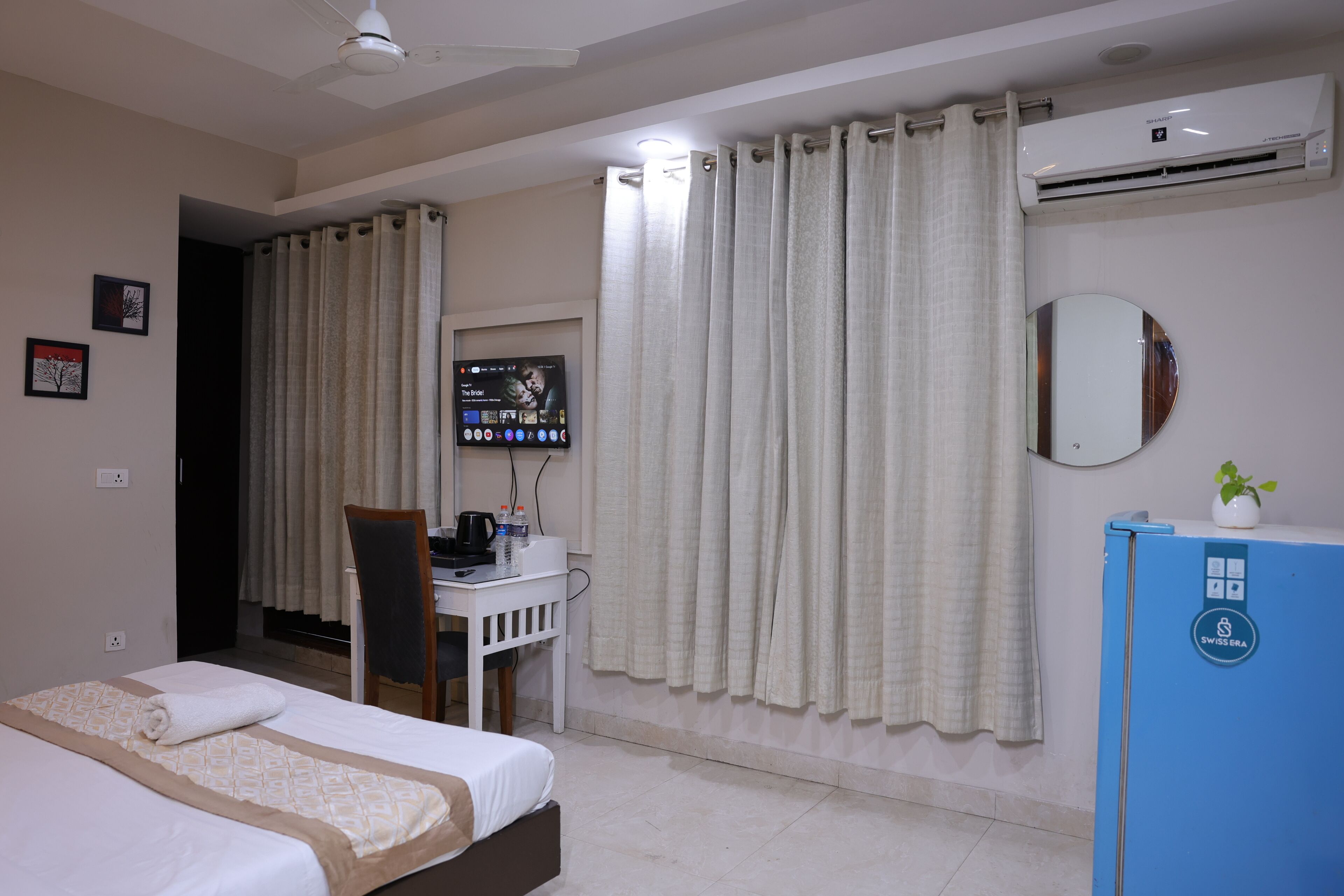 A hotel room with a bed, desk, chair, air conditioning unit, and a television.