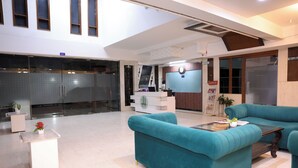 A modern interior with teal sofas, a white reception desk, and a kitchen area. - Hotel Zen Inn (New Delhi)