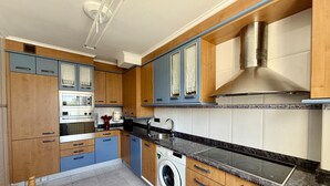 Une cuisine moderne avec des meubles en bois, un four encastré, un lave-linge et une hotte de cuisine en acier inoxydable.