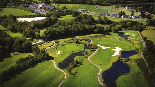A golf course with multiple bunkers, water hazards, and a clubhouse in the background.