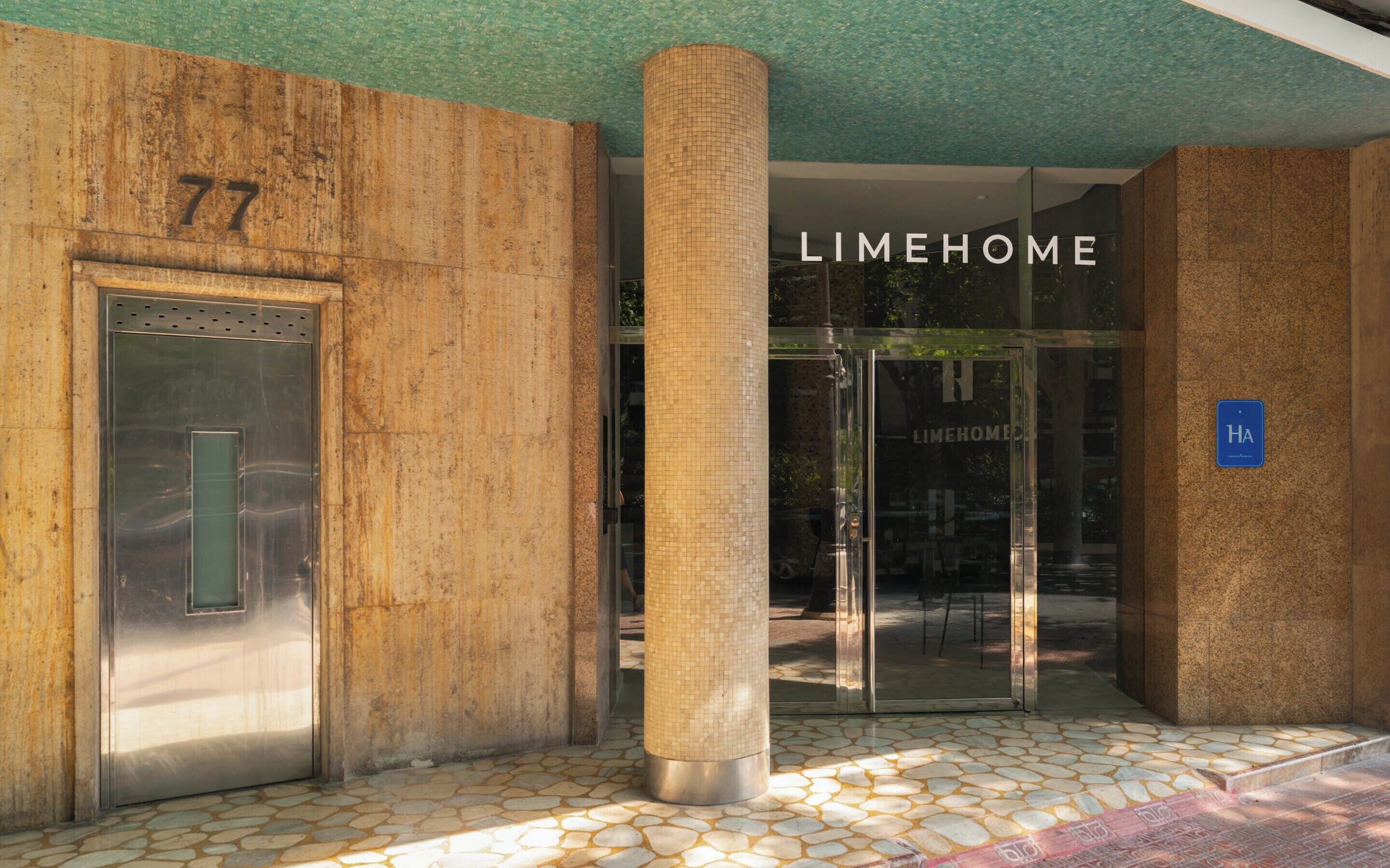 Ein Gebäudeeingang mit einer nummerierten Tür, einer Säule und einer Glastür mit der Beschriftung 'LIMEHOME'.