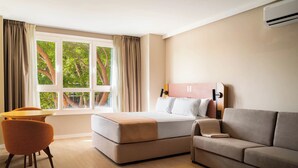 Una camera d'albergo con un letto, una poltrona, una sedia e una finestra con tende.
