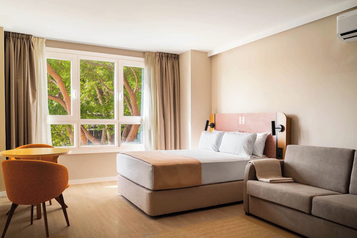 Una habitación de hotel con cama, sofá, sillón y ventana con cortinas.