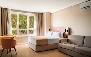 Quarto de hotel com uma cama, um sofá, uma cadeira e uma janela com cortinas.
