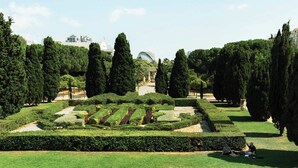 Un giardino curato con siepi ben tagliate, alberi alti e un percorso centrale che conduce a un edificio con una struttura a cupola.