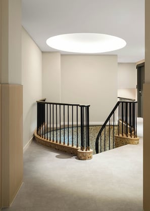 Uma escada com corrimão preto, luminária circular no teto e parede revestida com azulejos.
