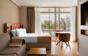 Een hotelkamer met een bed, een bank, een kleintje tafeltje, een televisie en een balkon met uitzicht op de stad.