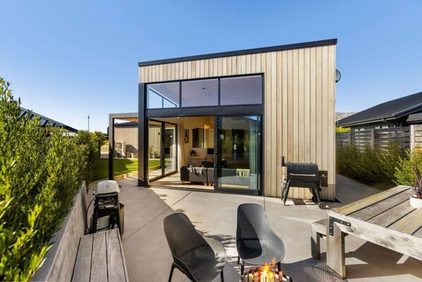 Ein modernes Haus mit Terrasse, Gartenmöbeln und einem Feuerkorb.