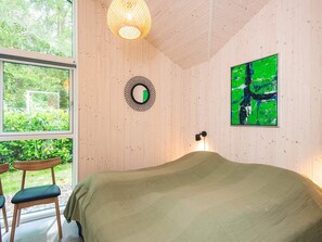 Una habitación con una cama, un espejo redondo, un cuadro abstracto verde y una ventana con vistas a la vegetación.