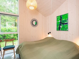 Una habitación con una cama, un espejo redondo, un cuadro abstracto verde y una ventana con vistas a la vegetación.
