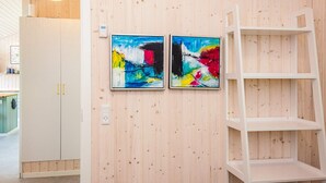 Quarto com paredes de painel de madeira, um guarda-roupa branco, duas pinturas abstratas coloridas e uma estante branca.