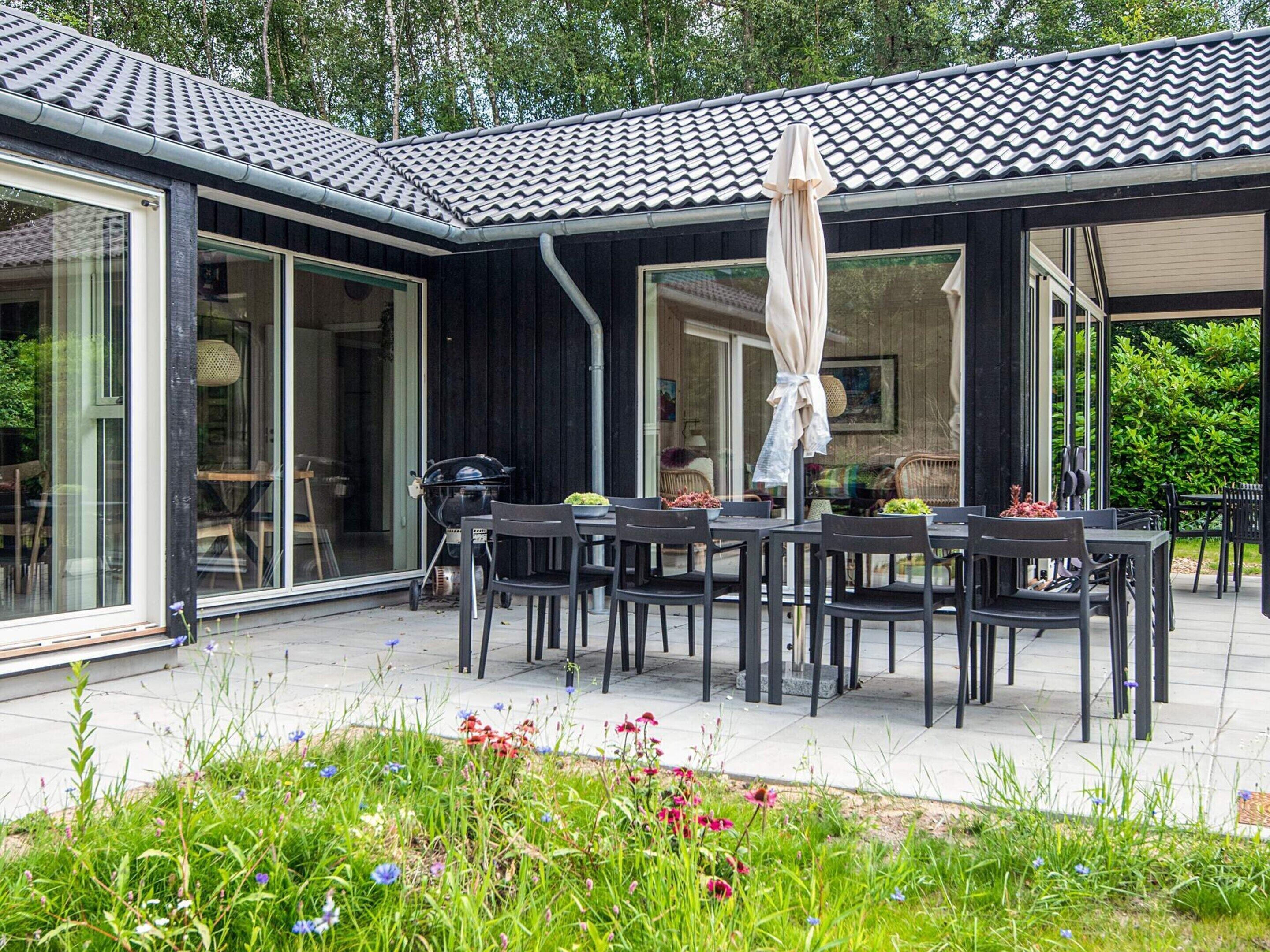 A covered outdoor dining area with tables and chairs, a grill, and a garden with flowers.