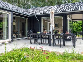 Un espacio al aire libre techado con mesas y sillas, una parrilla y un jardín con flores.