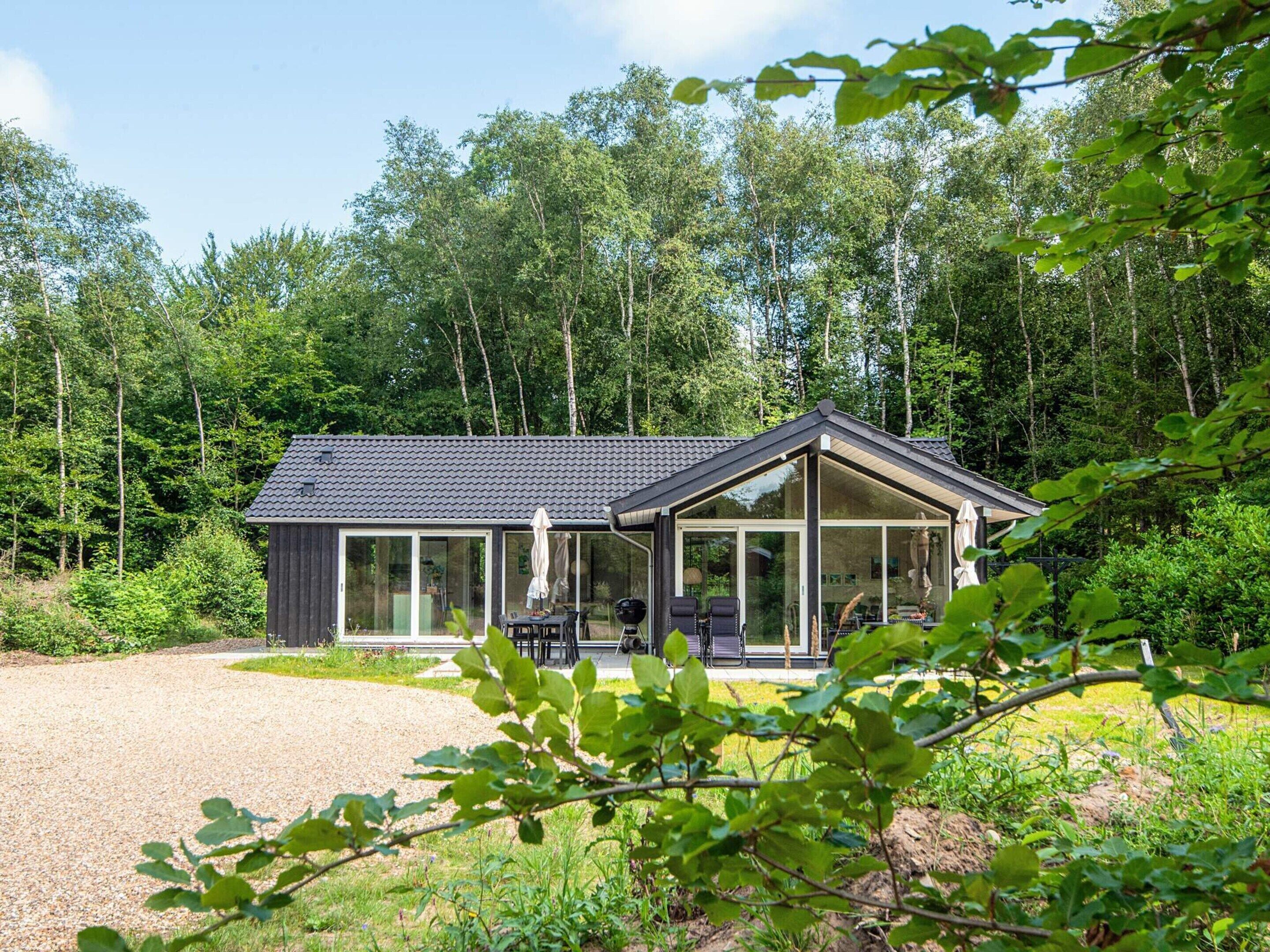Uma casa moderna com uma grande janela de vidro, rodeada por uma floresta.