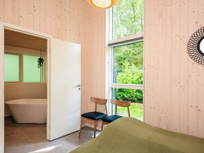 Ein Zimmer mit Holzwandverkleidung, einer Badewanne, zwei Sesseln und einem großen Fenster mit Blick auf Grünflächen.