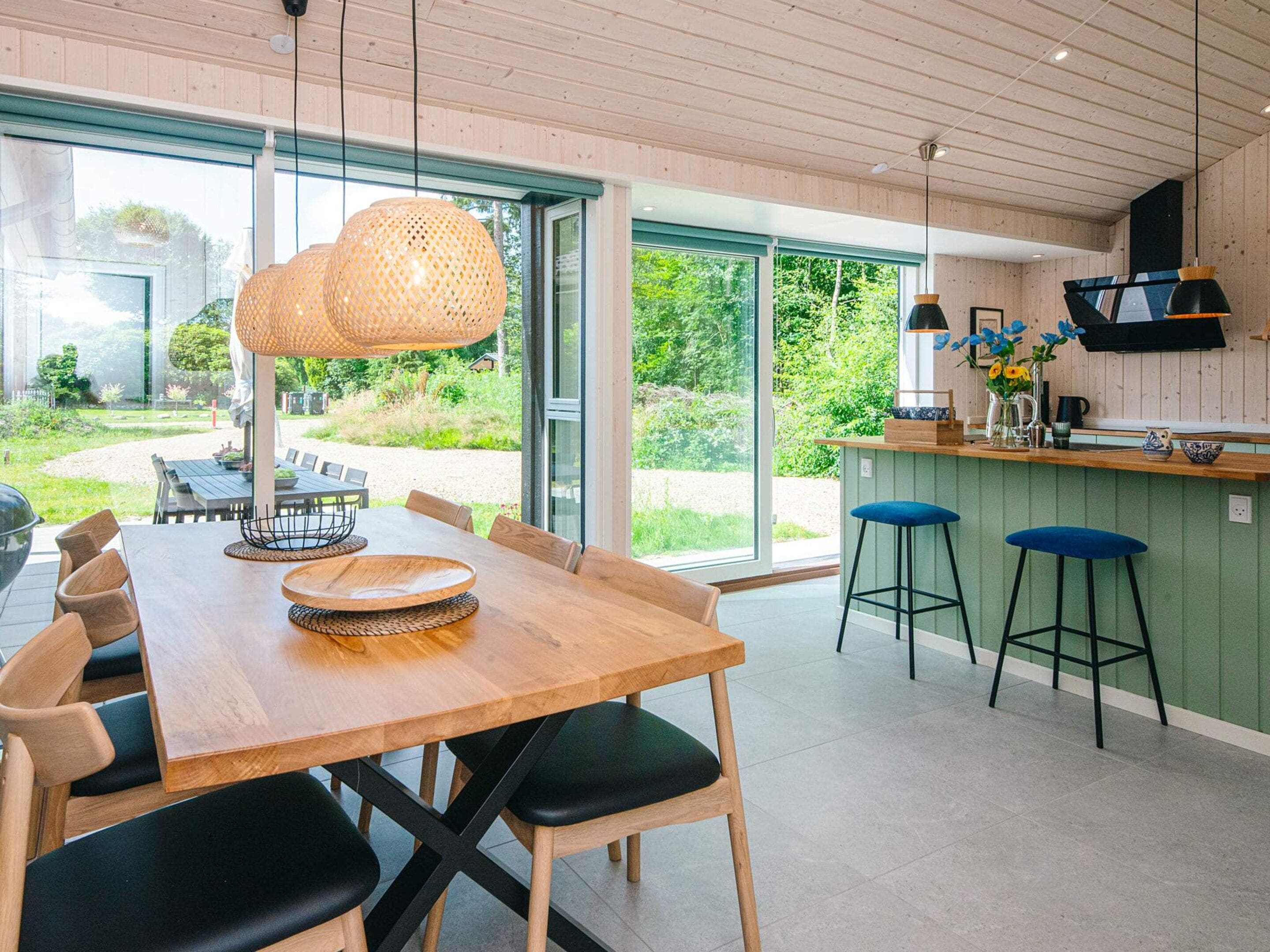 Een moderne keuken met een houten tafel, barstoelen, grote ramen en uitzicht op de omgeving.
