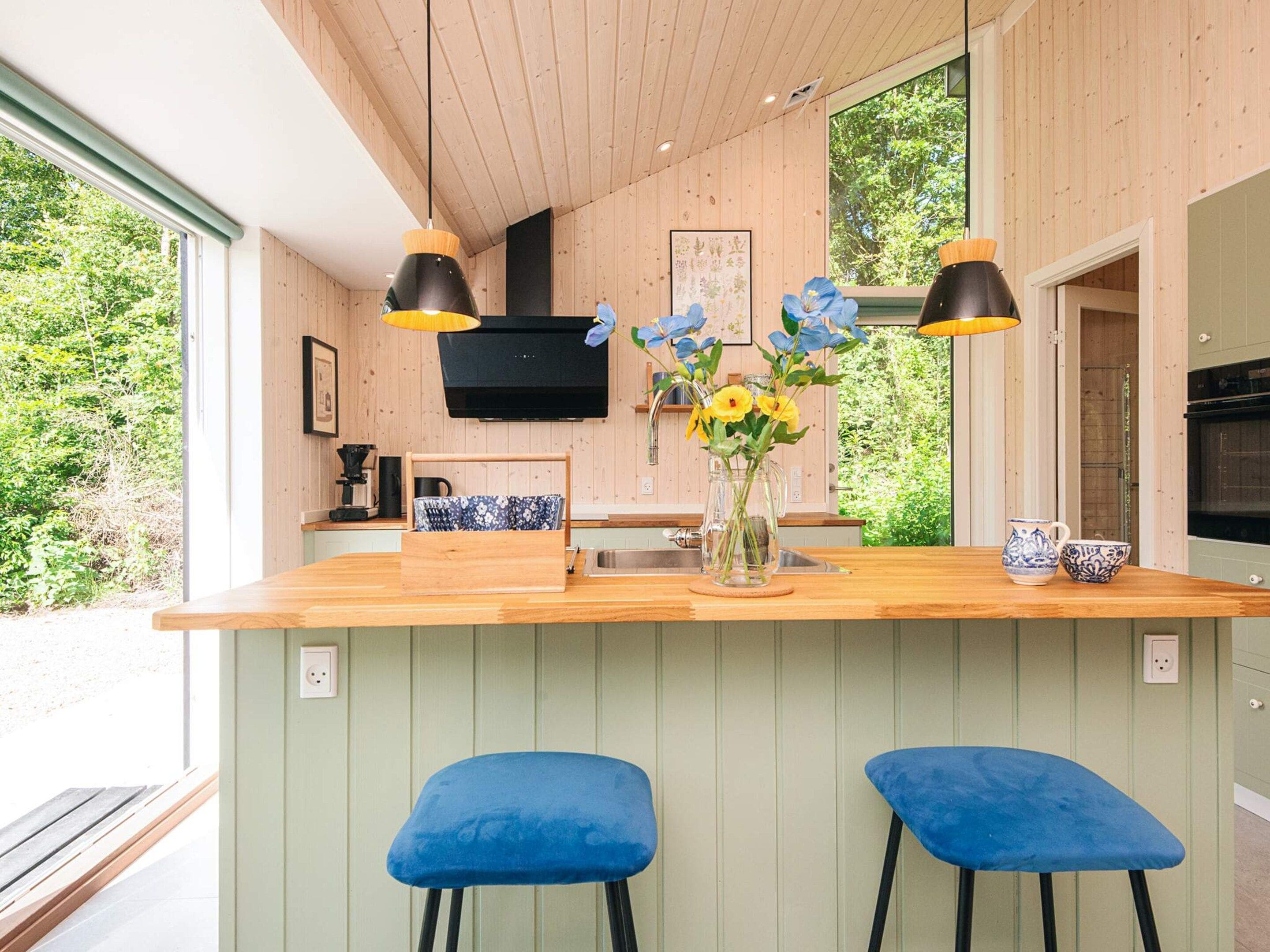 A modern kitchen with a wooden island, two blue bar stools, a vase with flowers, and a black range hood.
