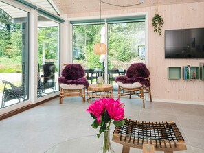 Ein modernes Interieur mit großen Fenstern, Korbmöbeln und einem Flachbildfernseher.