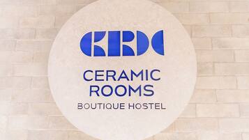 Een rond bord met de tekst 'CERAMIC ROOMS BOUTIQUE HOSTEL' voor een achtergrond van bakstenen.