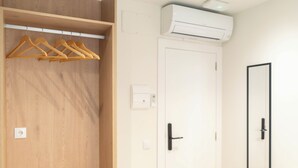 A wooden closet with wooden hangers, a white door with a black handle, and an air conditioning unit on the wall. - Ceramic Rooms Boutique Hostel (Villarreal)