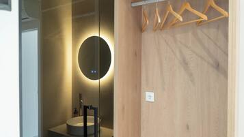 Un baño moderno con un espejo redondo, un lavamanos y perchas de madera en un perchero.