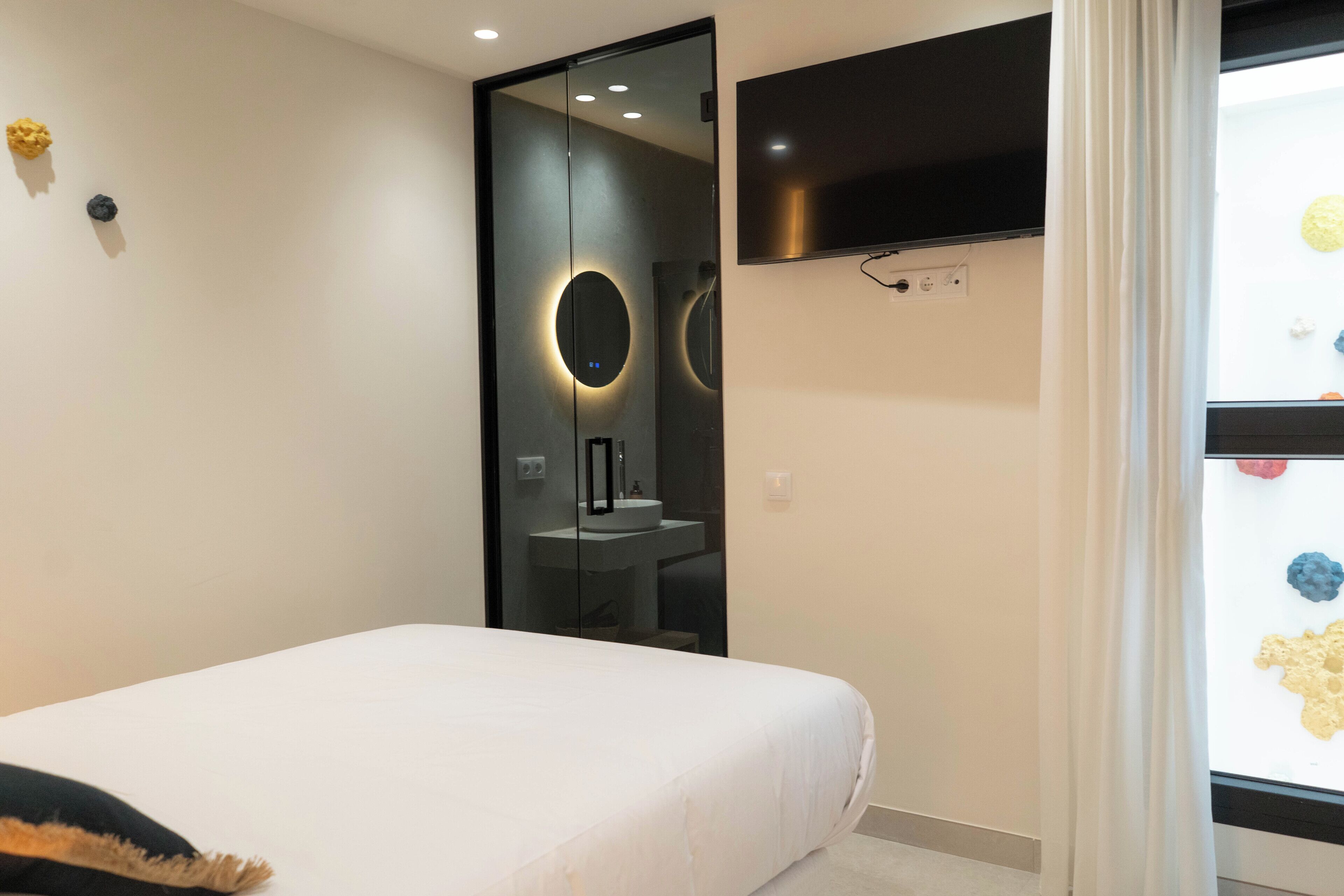 Un dormitorio moderno con cama, espejo, televisor y ventana con vistas al exterior.