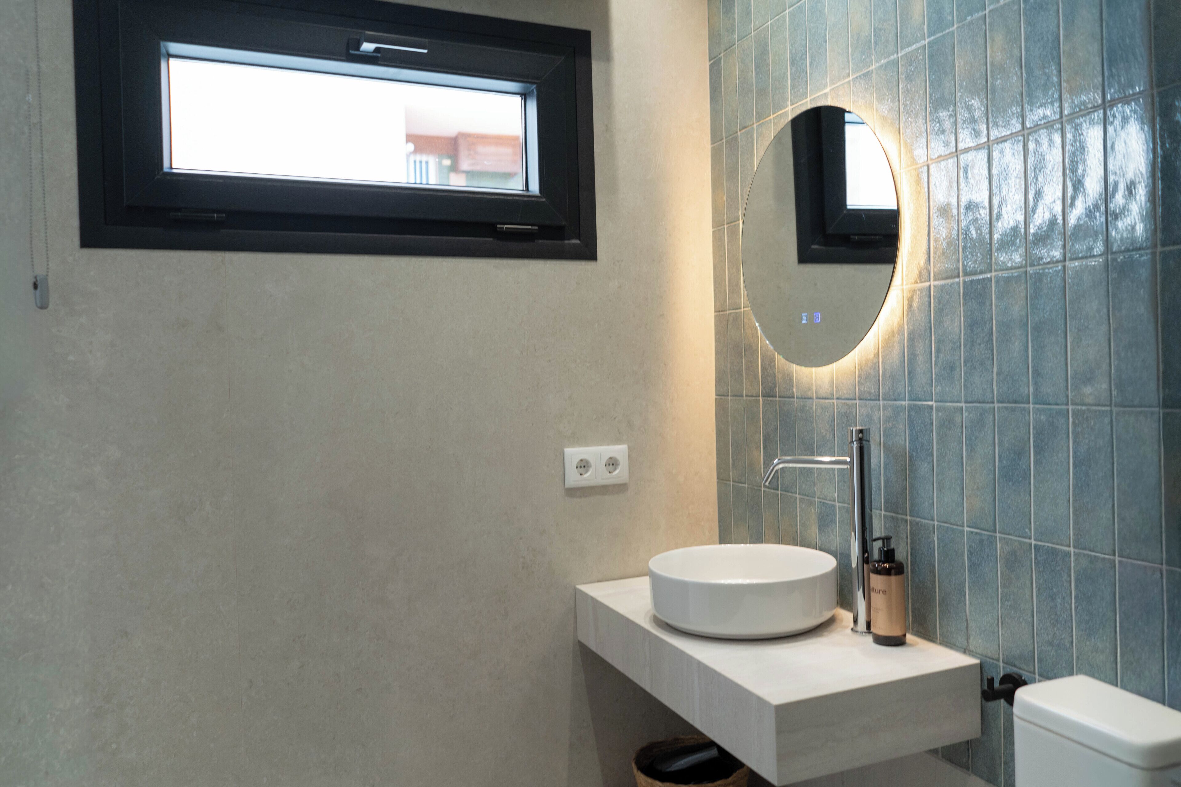 A bathroom with a round mirror, a window, and a sink.