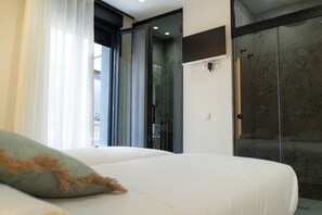 A modern hotel room with a bed, a glass shower enclosure, and a view of the outside. - Ceramic Rooms Boutique Hostel (Villarreal)