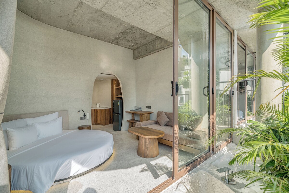 A modern bedroom with a bed, a wooden coffee table, a sofa, and a glass door leading to a balcony.