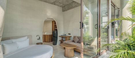 A modern bedroom with a bed, a wooden coffee table, a sofa, and a glass door leading to a balcony.