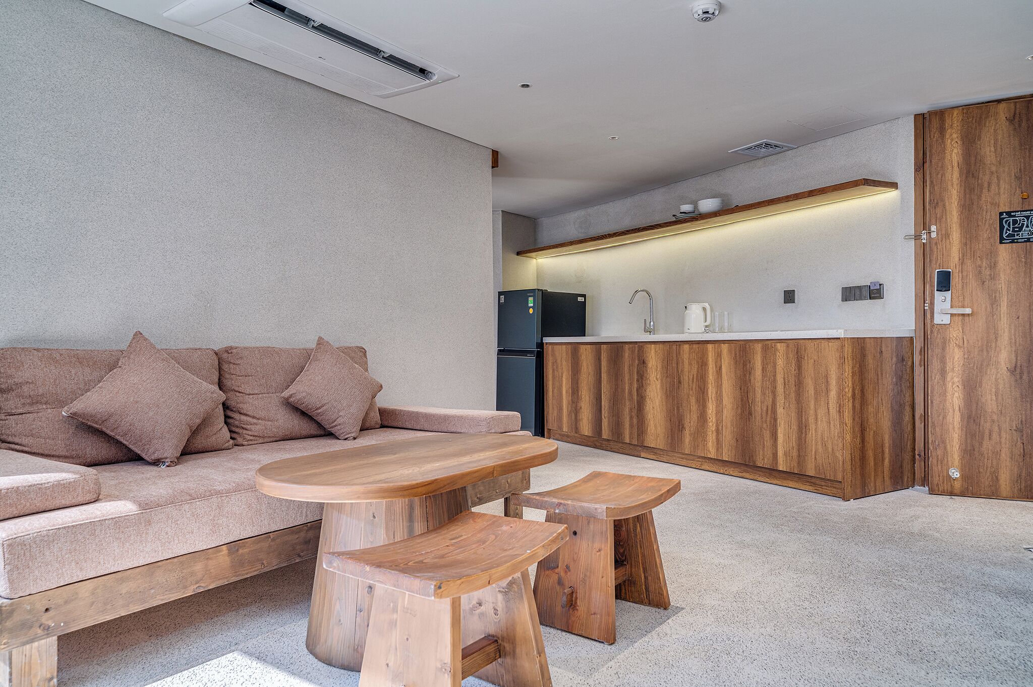 Een moderne woonkamer met een bank, een houten salontafel en krukken, een keuken met houten kastjes, en een deur met slot.