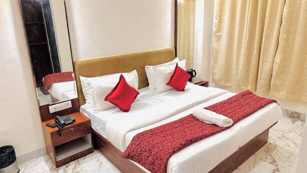 A hotel room with a large bed, a bedside table with a phone, a mirror, and a window with curtains. - Hotel Comfort Zone (Mumbai)