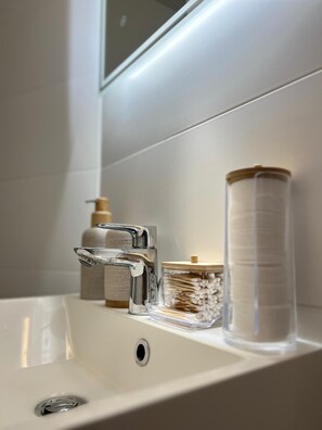 A bathroom sink with a chrome faucet, a soap dispenser, and a container of cotton swabs. - Charming cosy Studio in the heart of Aix - Ideal cocoon 🌿 (Aix-les-Bains)