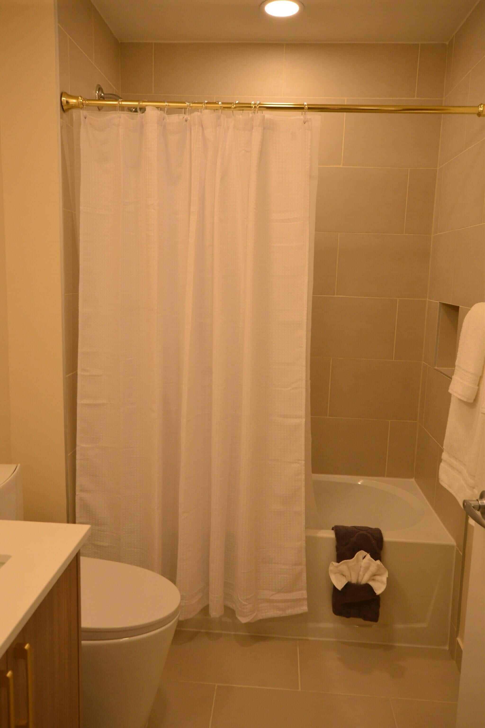 A bathroom with a shower curtain, a bathtub, a toilet, and a towel rack.