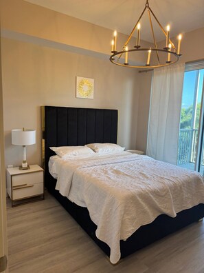 Ein Schlafzimmer mit einem großen Bett, einem Nachttisch mit Lampe, einer Chandelierleuchtre und einem Fenster mit Vorhängen.