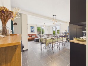 A spacious dining area with a long table and chairs, a kitchen with dark cabinets, and a living area with a sofa and a painting. - 950m from the sea - family home with garden (Piriac-sur-Mer)
