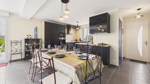 Una cucina moderna con zona pranzo, caratterizzata da una grande isola, mobili a parete scuri e luci a sospensione.