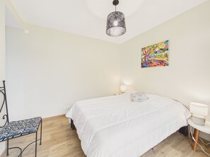 Et soveværelse med en seng, stol, skrivebord, lampe og et billede på væggen.