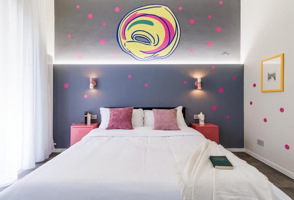 A bedroom with a bed, two bedside tables, a wall with a colorful circular design, and a framed picture on the wall.