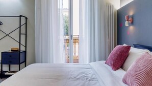 Un dormitorio con cama, mesita de noche, ventana con cortinas e iluminación en la pared.