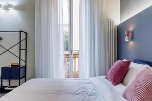 Ein Schlafzimmer mit einem Bett, einem Nachttisch, einem Fenster mit Vorhängen und einer Wandleuchte.