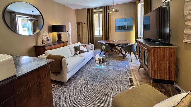 Une chambre d’hôtel équipée d’un canapé, d’une table à manger, de chaises, d’un téléviseur, d’un miroir et d’un tapis à motifs.