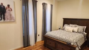 A bedroom with a wooden bed, grey curtains, a painting on the wall, and a wooden floor. - Apartment in downtown Newark, walking to Penn Sta. (Newark)