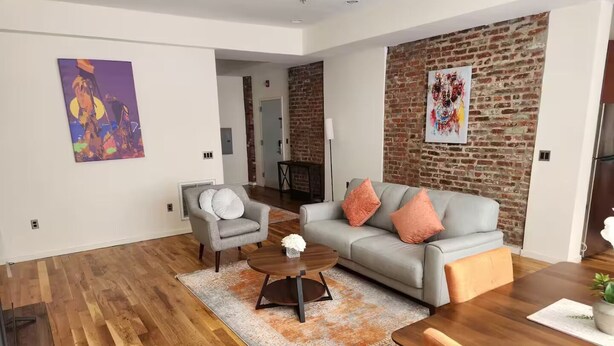 A modern living room with a grey sofa, a coffee table, and a dining area with a wooden table and chairs. - Apartment in downtown Newark, walking to Penn Sta. (Newark)